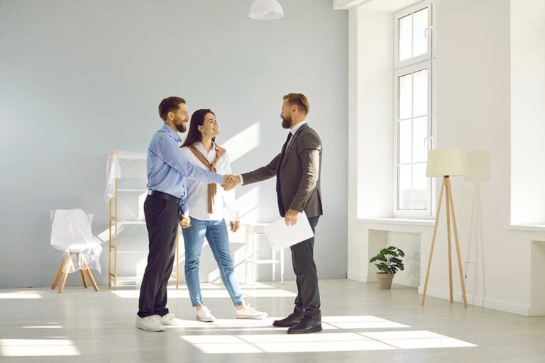 A couple reviews real estate documents with an agent at a kitchen table beside a laptop and notepad.